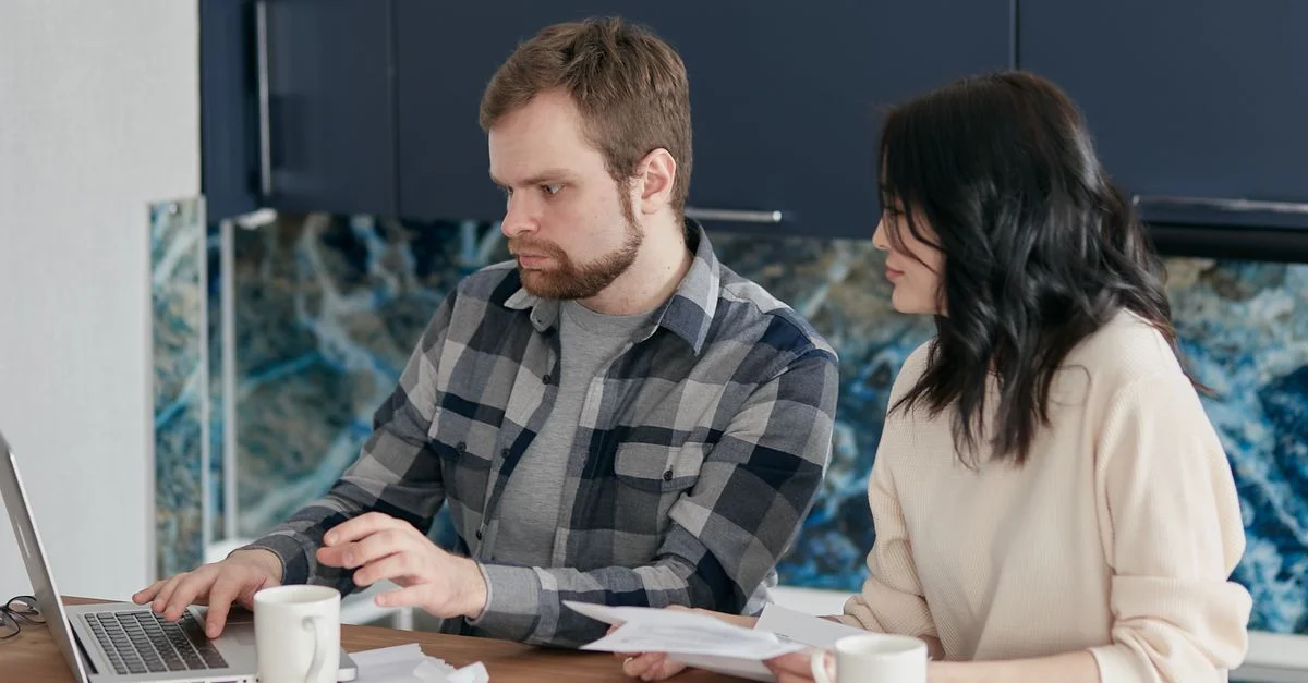 Un couple travaillant ensemble sur un ordinateur portable pour gérer les finances à la maison, mettant en avant le travail d'équipe et la concentration.