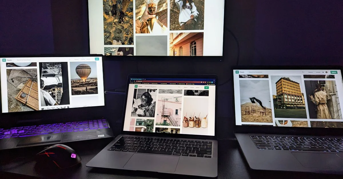 Trois ordinateurs portables et un moniteur sur un bureau affichant des designs graphiques créatifs. Parfait pour des projets axés sur la technologie.