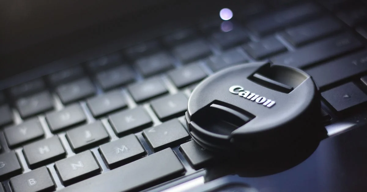 Gros plan sur un capuchon d'objectif Canon posé sur un clavier d'ordinateur portable, mettant en avant la technologie moderne.