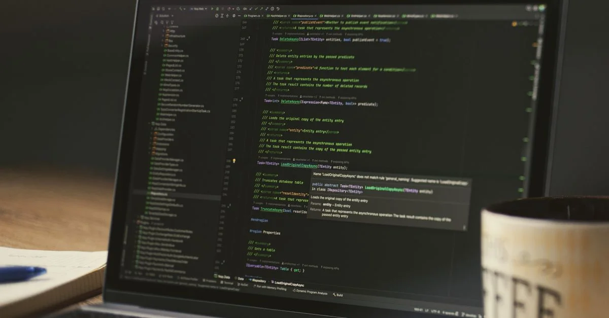 Un gros plan d'un ordinateur portable affichant du code dans une pièce faiblement éclairée avec une tasse de café à proximité.